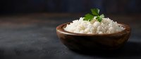 Cooked white rice in wooden bowl garnished with fresh parsley on dark slate surface. Healthy grain side dish for Asian cuisine and meal preparation.