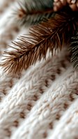 Brown pine branch against soft white knitted texture creates cozy winter mood. Natural seasonal composition with selective focus and bokeh effect.