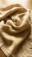 Soft beige linen fabric with natural wrinkles and folds creating organic texture on wooden surface for home decor and textile design projects.