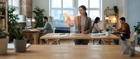 Diverse team of professionals collaborating in modern office workspace with natural light, plants, and digital technology for business projects and teamwork.
