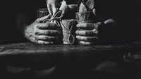 Elderly craftsman hands working with traditional rope and tools on wooden surface in dramatic black and white lighting for artisan projects.