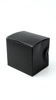 Black glossy cube-shaped gift box with ribbon handle isolated on white background for packaging and retail display purposes.