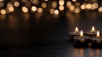 Diwali oil lamps burning on dark wooden surface with warm golden bokeh lights background creating festive atmosphere for Hindu celebration.