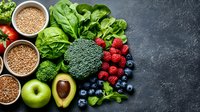 Fresh organic superfoods on dark stone background with copy space. Healthy eating ingredients including berries, grains, avocado, broccoli and leafy greens.