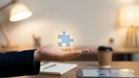 Business hand holding glowing puzzle piece in modern office workspace representing solution finding and problem solving for corporate strategy.