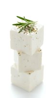 Stacked white cheese cubes with herbs and spices, isolated on white background, ready for culinary and food design projects.