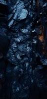 Dramatic dark blue rocky cliff face with jagged formations and subtle warm light accents creating mysterious atmosphere. Natural geological texture background.