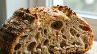Freshly baked artisan sourdough bread loaf with open crumb structure, crusty exterior, and rustic scoring marks, ideal for bakery, food, and culinary content.
