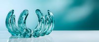 Clear blue glass decorative bowl with flowing wave-like design on white surface against turquoise background for modern home decor and interior styling.