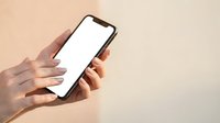 Female hands holding smartphone with blank white screen against neutral beige background, suitable for app mockups, mobile technology marketing, and digital interface presentations.