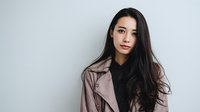 Young Asian woman with long dark hair wearing pink leather jacket and black top against light gray background, portraying confidence and modern style.