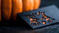 Ornate black leather wallet with decorative floral embossing pattern detail in dramatic lighting with orange pumpkin background, showcasing luxury craftsmanship and seasonal mood.
