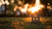 Wooden house silhouette on grass at sunset with golden bokeh background, symbolizing home, real estate, and family comfort.