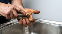 Dirty male hands scrubbing with a brush over a stainless steel sink, showing hard work and manual labor hygiene routine.