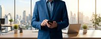 Professional businessman in navy suit using smartphone in modern office with city skyline view during golden hour sunset lighting.