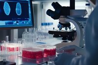 Laboratory research with microscope and red cell samples in petri dishes. Computer screen shows medical analysis results in modern scientific facility.