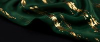 Luxurious emerald green silk fabric with golden foil accents flowing in elegant waves, premium textile material for fashion and interior design projects.