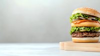 Fresh juicy burger with beef patty, cheese, tomato, lettuce and onion rings on wooden cutting board against light gray background. Perfect for menu design.