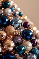 Festive arrangement of shiny and glittery Christmas baubles in navy blue, gold, silver, and purple with soft bokeh lights creating magical holiday atmosphere.
