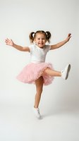 Happy young girl with pigtails jumping in pink tulle skirt and white shirt on neutral background. Joyful child expressing excitement and energy.