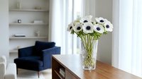 White anemone flowers in crystal vase on wooden table in modern living room with navy blue armchair and built-in shelves for home decor and interior design.