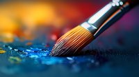 Paint brush with natural bristles dipping into blue oil paint against vibrant orange and purple background, macro photography showing artistic texture and detail.