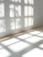 Sunlight streaming through window creates geometric shadow patterns on white wall and wooden floor in minimalist empty room interior space.