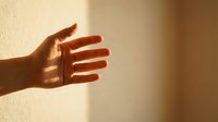 Close-up of an open hand casting a shadow on a neutral wall, conveying concepts of light, gesture, communication, and minimalist design for creative projects.