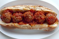 Homemade meatball submarine sandwich with marinara sauce on fresh Italian roll, served on white plate, close up view of classic comfort food preparation.