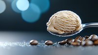 Creamy coffee ice cream scoop on spoon with roasted coffee beans scattered on reflective surface against blurred blue bokeh background.