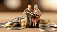 Senior couple figurines sitting on stacks of coins reading financial documents together representing retirement planning and pension savings.