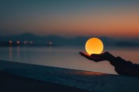 Hand holding glowing orb at sunset over calm water creating magical silhouette scene for meditation wellness and spiritual concepts.