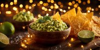 Fresh guacamole dip in wooden bowl with tortilla chips and lime on dark table with festive bokeh lights in background.