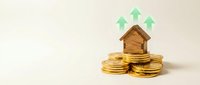 Wooden house model on golden coins with green upward arrows showing real estate investment growth and property value increase concept.