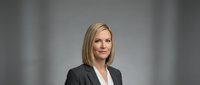 Confident Caucasian businesswoman in gray blazer posing for professional corporate headshot against neutral studio background.