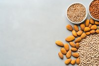 Raw almonds, chickpeas, lentils and other legumes scattered on grey concrete background with copy space, top view of healthy plant protein sources.
