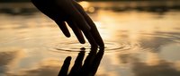 Hand touching water surface creating ripples at golden hour sunset, suitable for wellness, spirituality, mindfulness and environmental concepts.