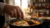 Professional chef hand stirring colorful vegetable stew in cast iron pan during golden hour cooking session in rustic kitchen with warm ambient lighting.