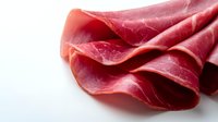 Thinly sliced prosciutto ham arranged in delicate folds on white background, showing marbled texture and rich red color. Premium cured meat for gourmet food design.