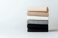 Neatly folded stack of minimalist towels in neutral colors from black to beige arranged on white background, showing texture and layers of fabric.
