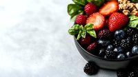Fresh mixed berries with strawberries, blueberries, blackberries, and raspberries in black ceramic bowl on light concrete background with green basil leaves.