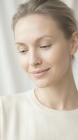 Young Caucasian woman with natural makeup and glowing skin in white sweater looking down peacefully for skincare and wellness concepts.