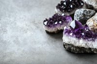 Natural amethyst crystal geodes with purple druzy formations on textured stone surface for healing meditation and spiritual wellness practices.