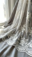 Elegant lace curtains with floral embroidery draping by a bright window, featuring delicate rose patterns and ornamental details for home decor and interior design.