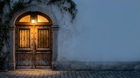 Rustic wooden door with warm light glowing through arched entrance in Mediterranean style building at dusk creating cozy atmospheric scene for hospitality design.