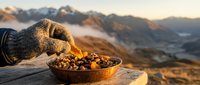 Hiker pouring trail mix from wool glove into bowl at mountain summit during golden hour with alpine valley landscape below.