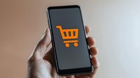 Hand holding smartphone with orange shopping cart icon on screen for mobile commerce and online retail applications.