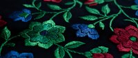 Vibrant embroidered floral pattern with colorful flowers and leaves on dark fabric. Traditional needlework design for textile and fashion applications.