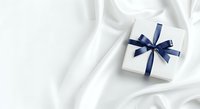 Wrapped gift box with navy blue ribbon bow on white silk fabric background, suitable for holiday, celebration, and greeting card designs.