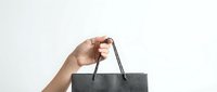 Hand holding gray shopping bag with black handles against white background for retail and consumer concepts.